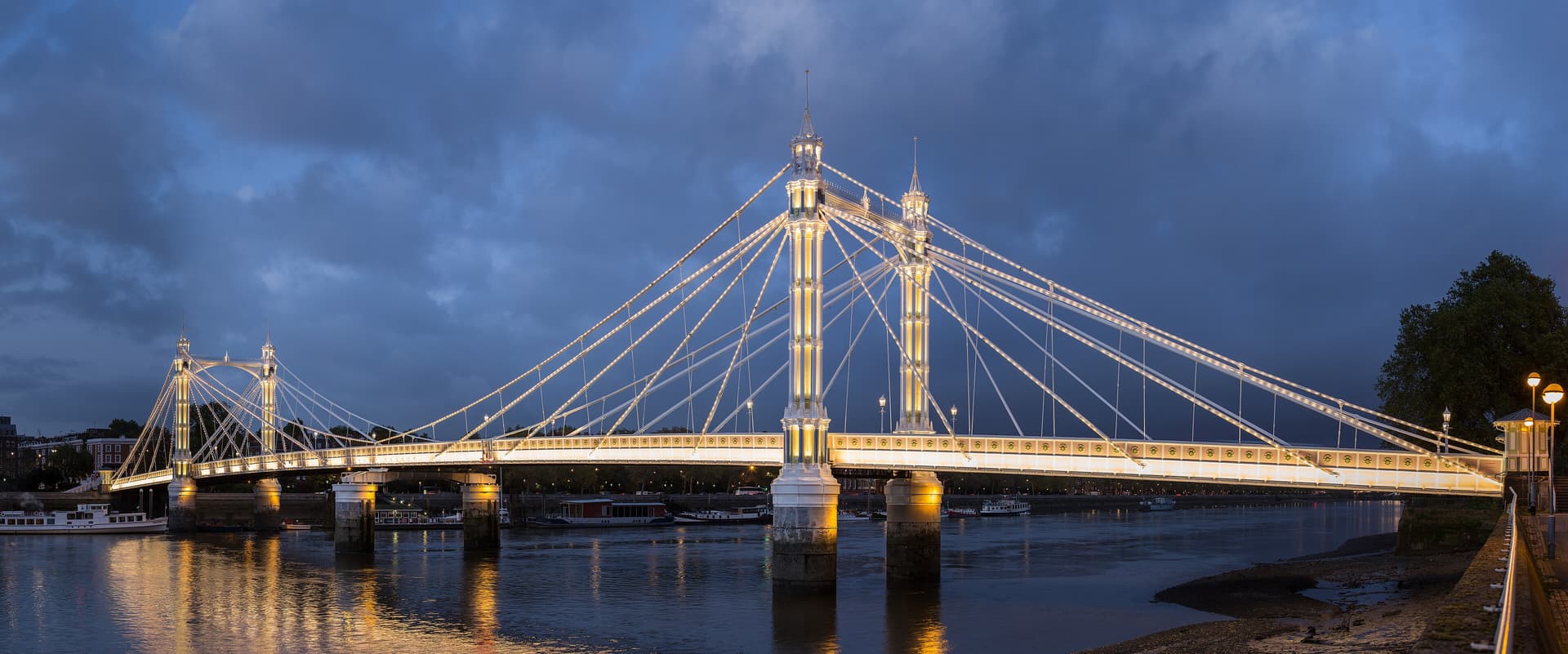 Albert Bridge lit up at dusk, its suspension cables and towers glowing above the Thames