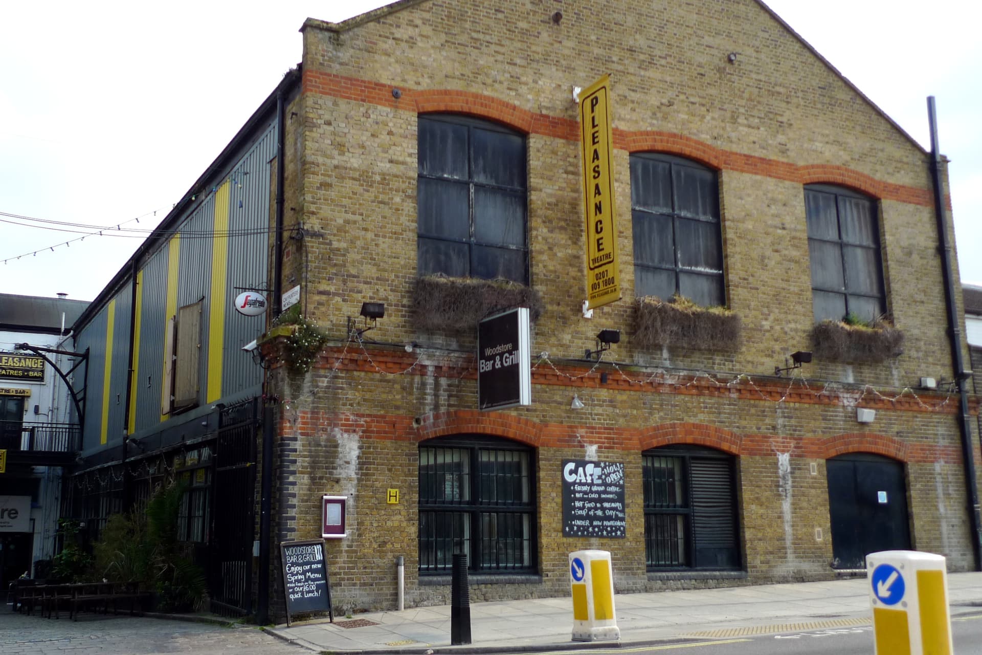 Yellow stock brick building with red brick arches and a hanging Pleasance Theatre banner on a London street