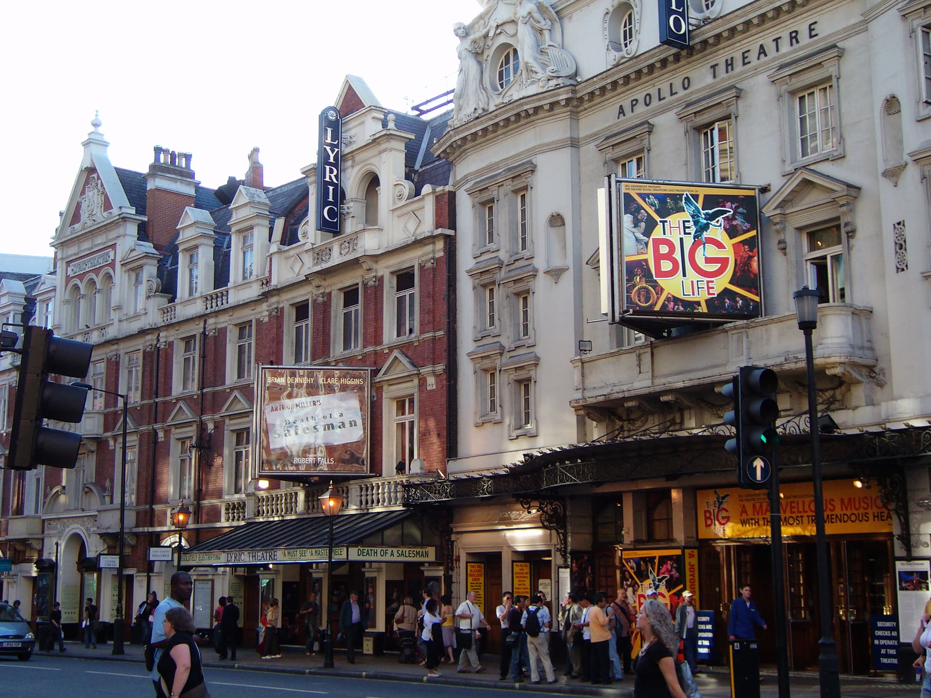 Apollo and Lyric theatres on Shaftesbury Avenue, with ornate facades, illuminated billboards and pedestrians passing along the pavement