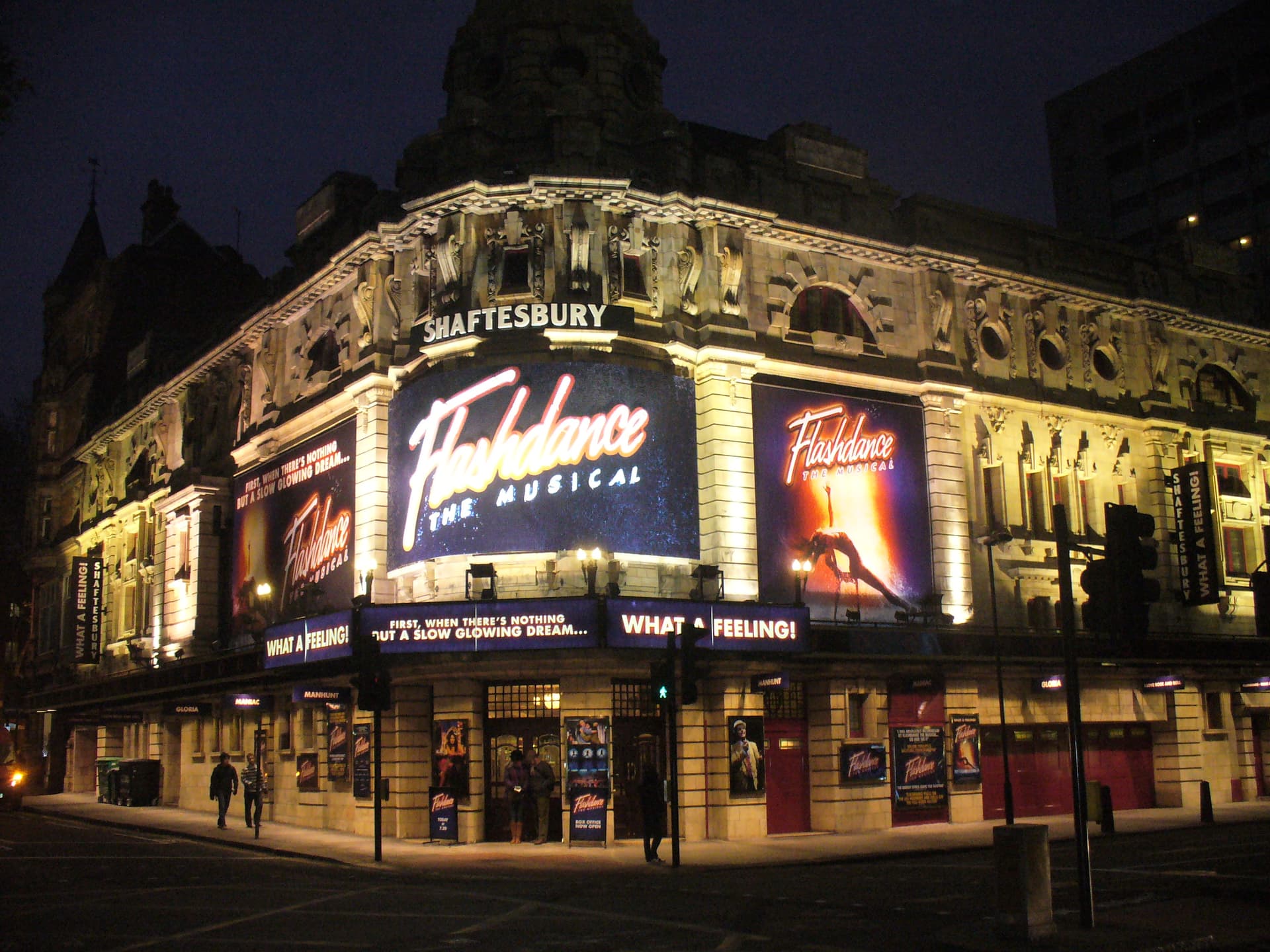 Shaftesbury Theatre corner facade lit up at night with Flashdance The Musical billboards above the entrance