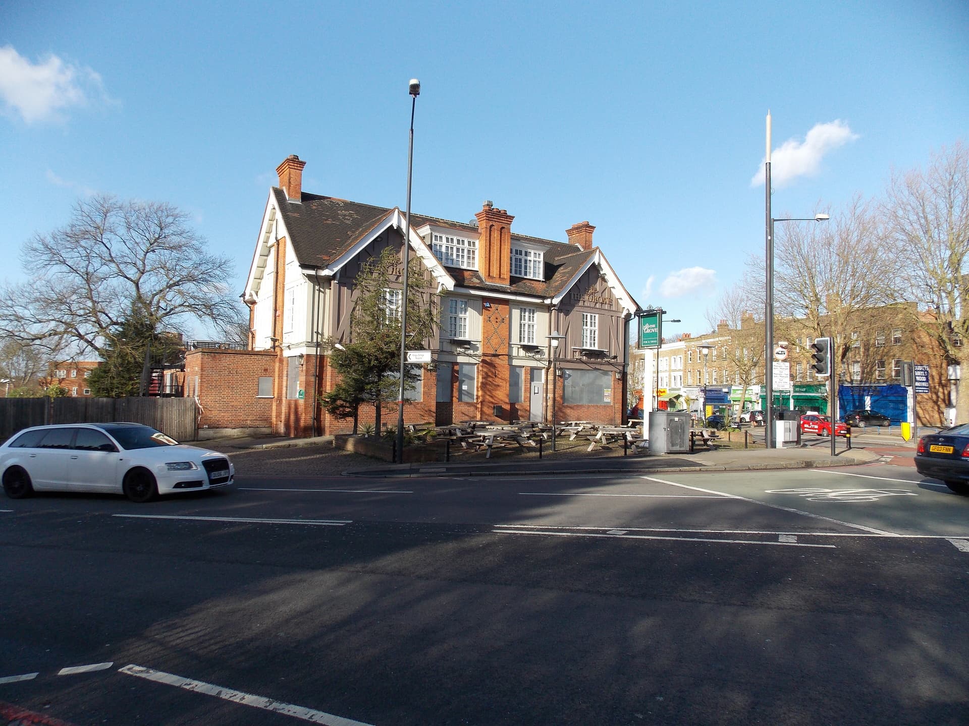 Boarded-up red-brick and timber-framed pub called The Grove on a London street corner with empty picnic benches