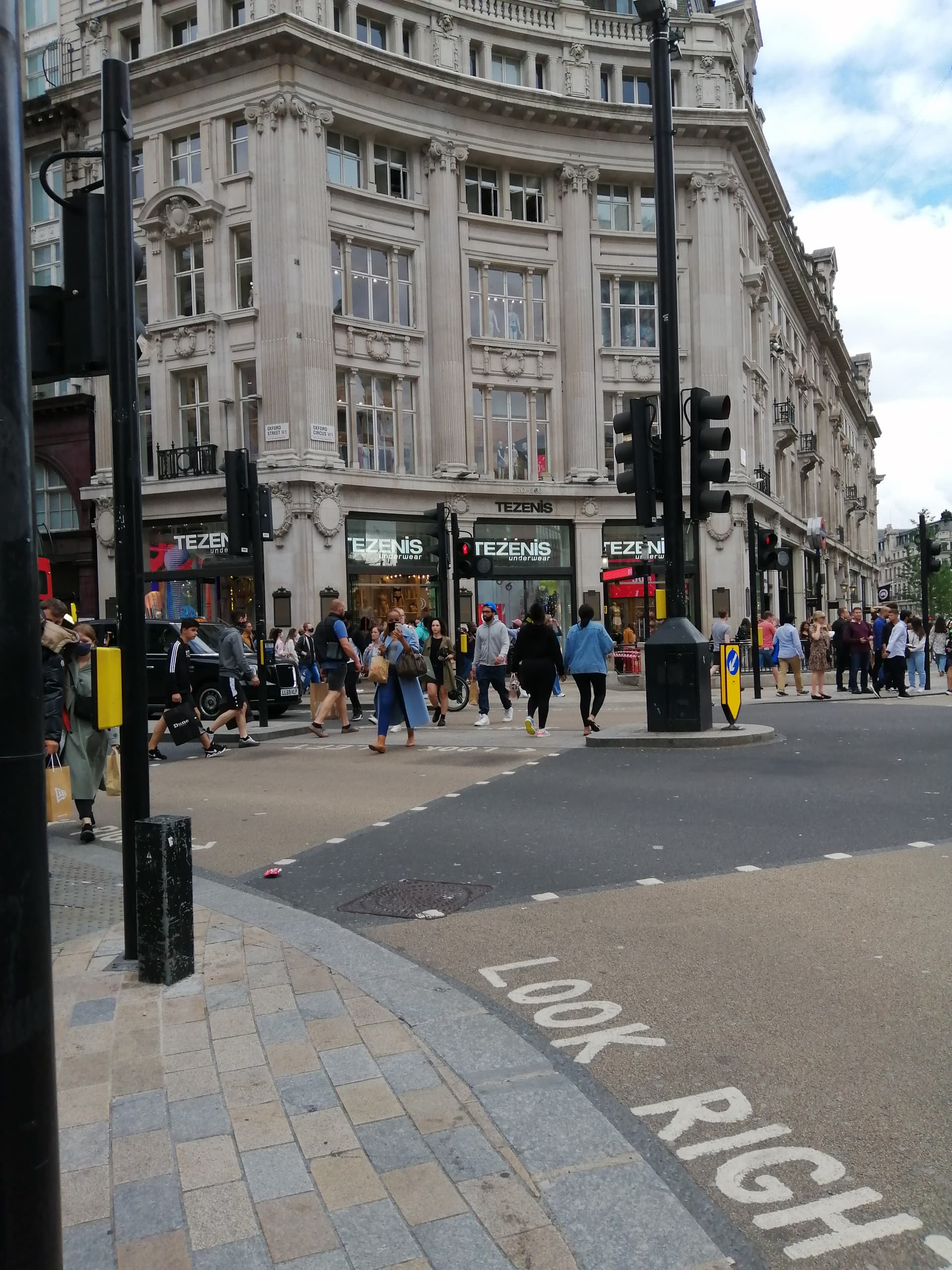 Pedestrians crossing the junction at Oxford Circus beneath a grand stone corner building with shopfronts and traffic lights