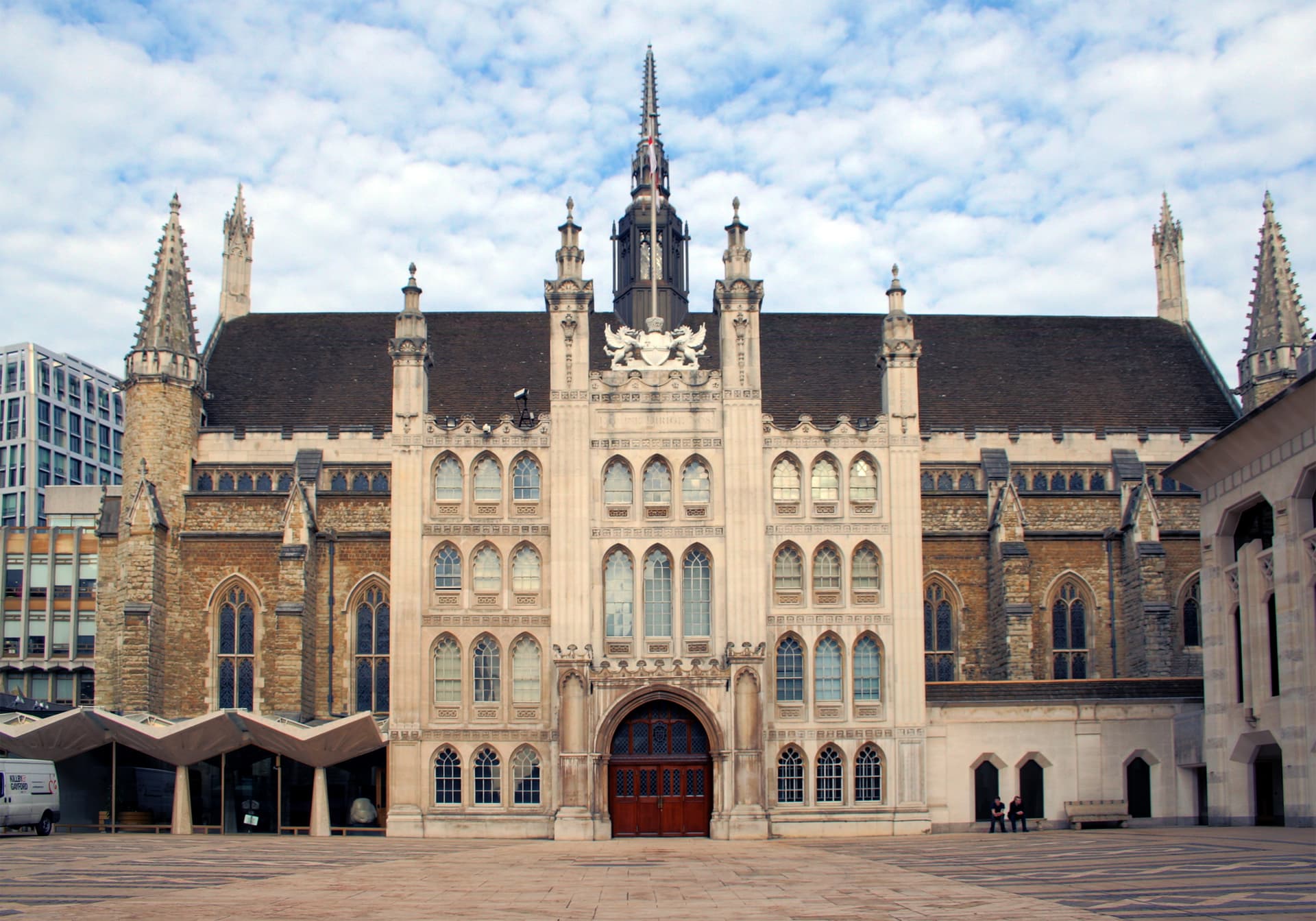 Gothic stone facade of Guildhall in the City of London with spires, arched windows and a paved yard