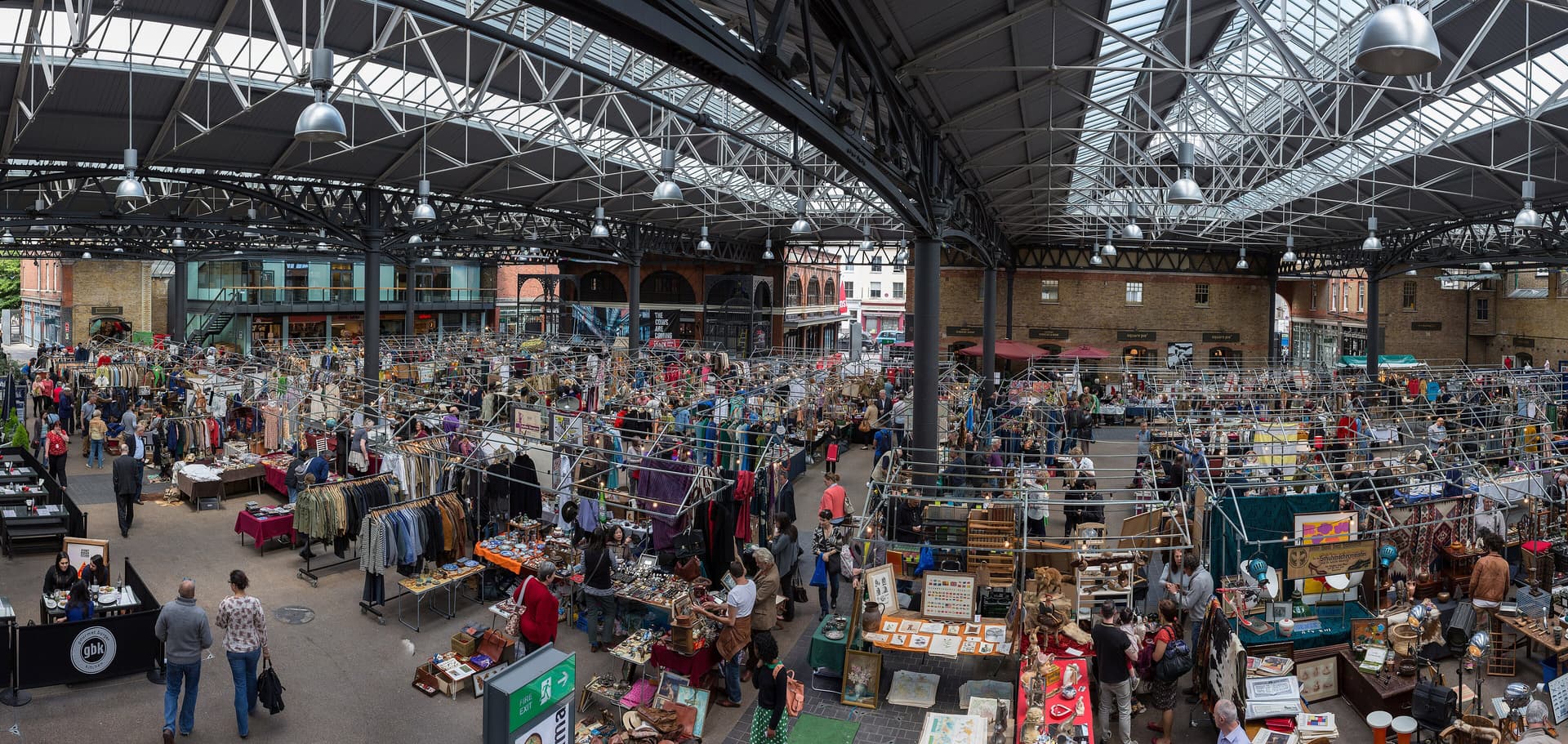 Wide view inside Old Spitalfields Market, with antique and clothing stalls beneath a steel and glass roof