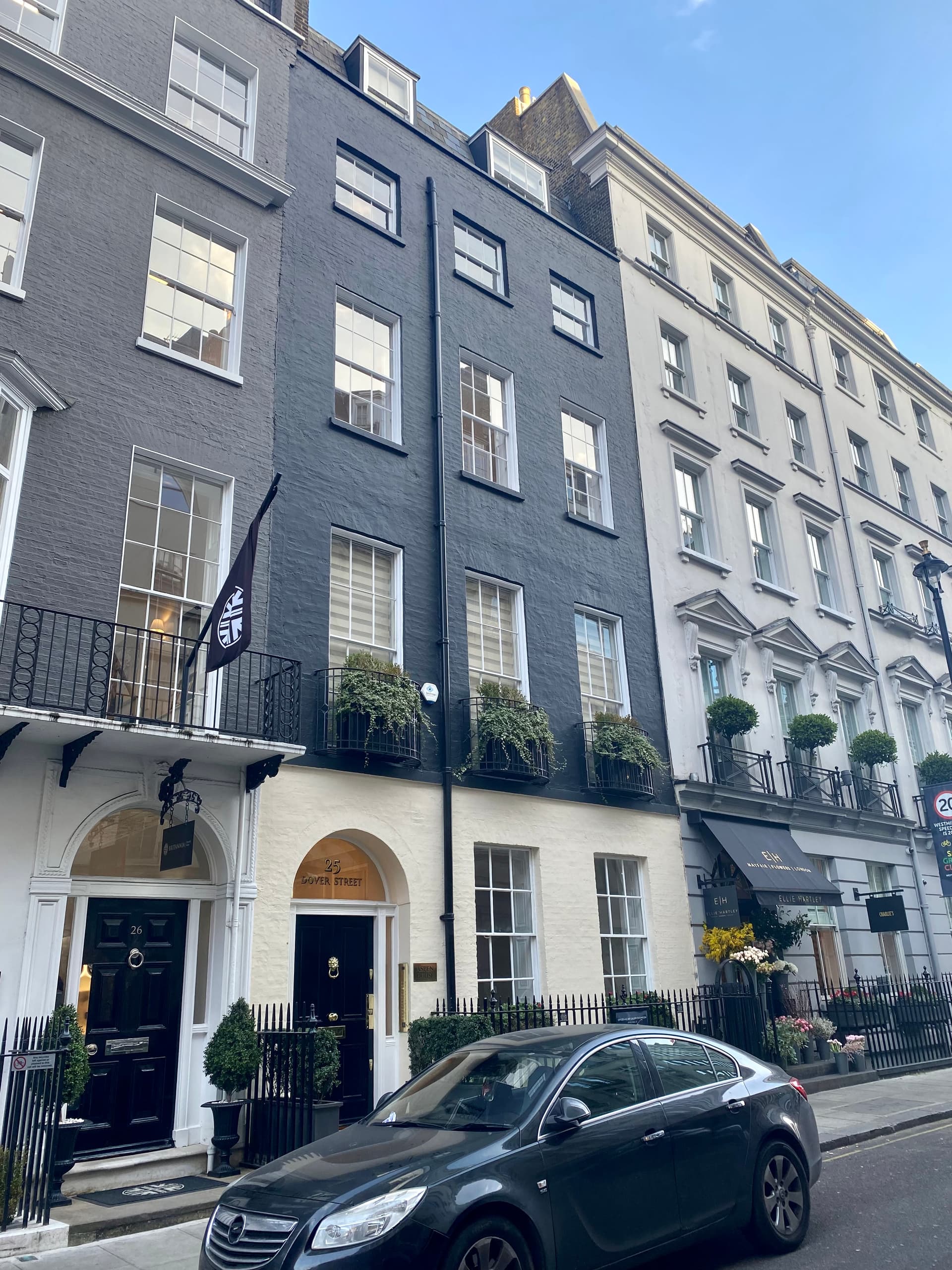 Georgian terraced townhouses on Dover Street, Mayfair, with a dark painted brick facade, balconies with planters and a parked car