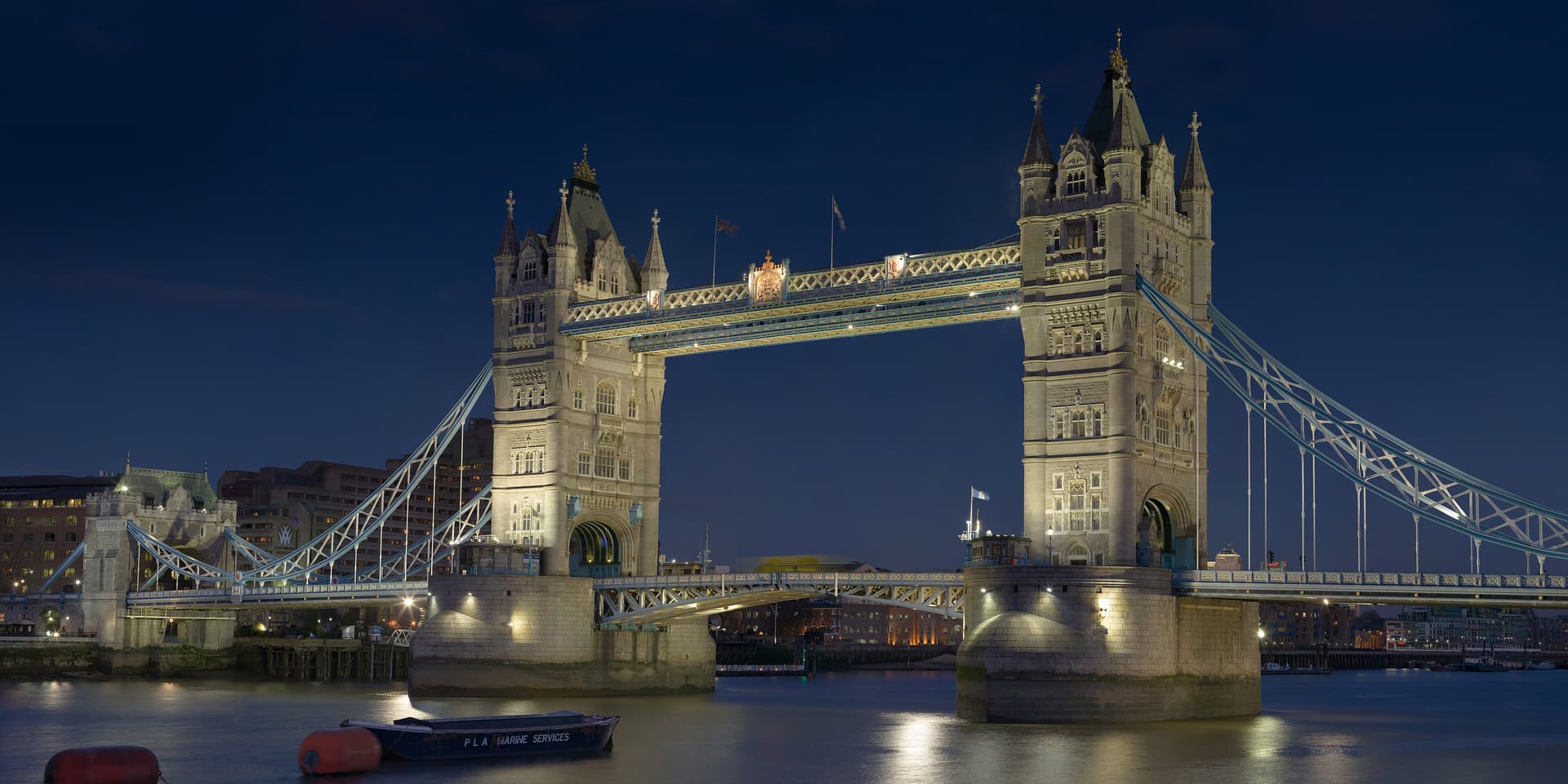 Tower Bridge illuminated at dusk with the Thames in the foreground and a small boat moored on the water