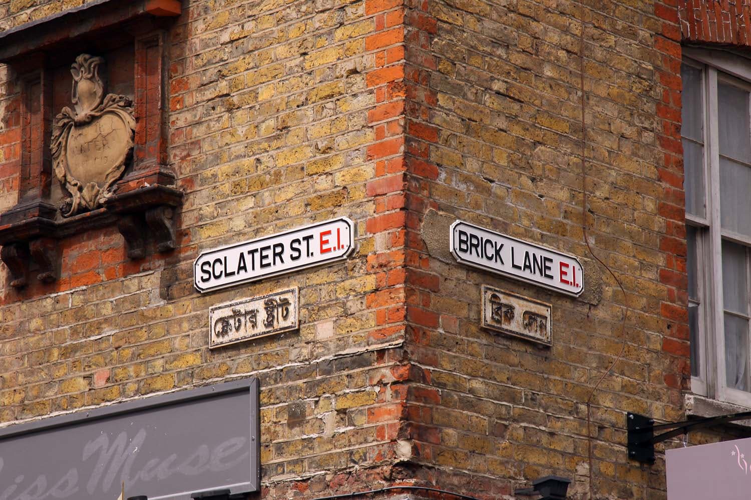 Street name signs for Sclater Street and Brick Lane in English and Bengali on a yellow brick corner