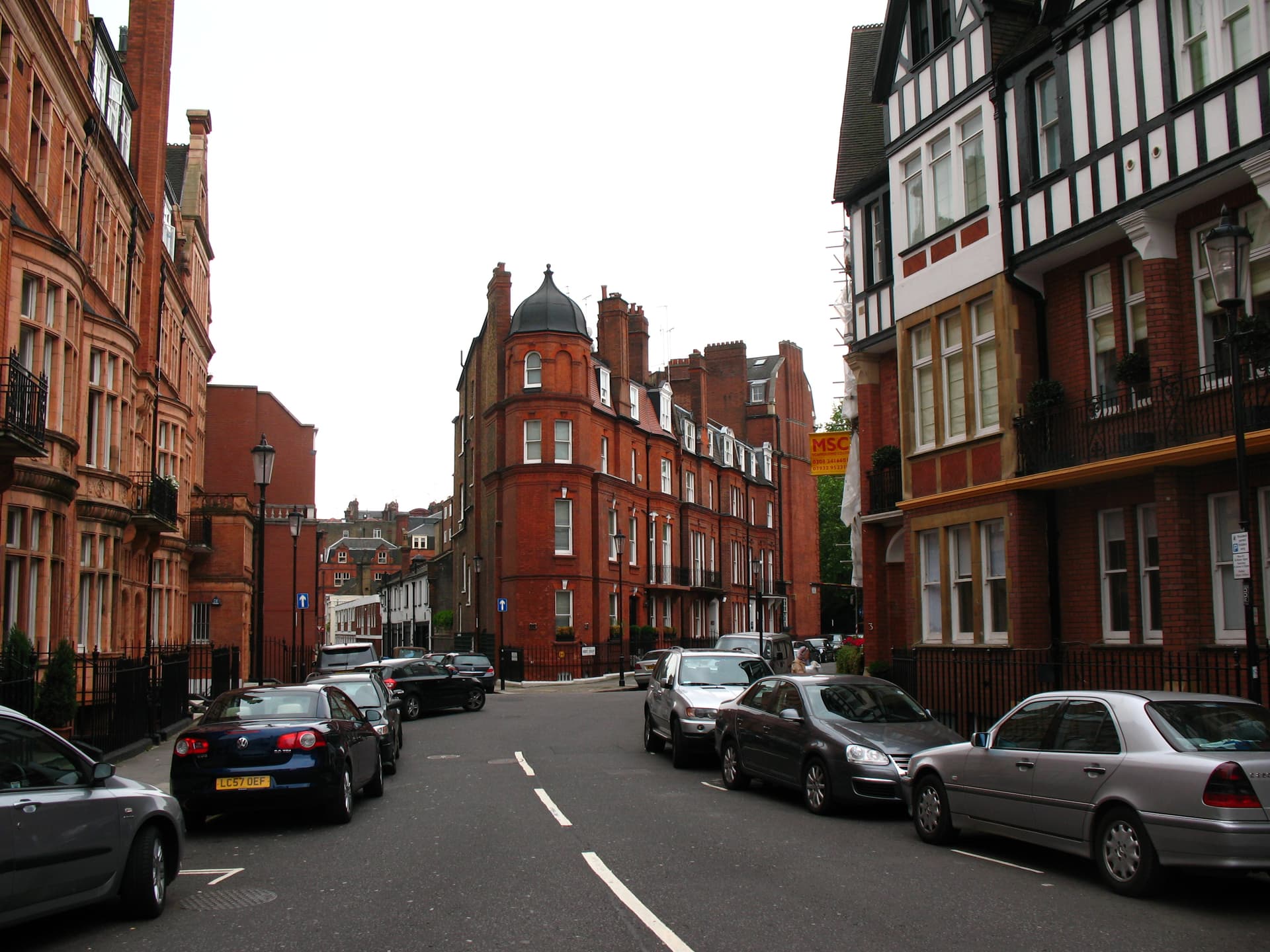 Quiet London street lined with red brick Victorian mansion blocks, a domed corner turret and parked cars